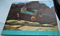 Full view of the vintage surreal print featuring a rusty blue pedal car flying over a canyon landscape with text below.