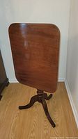 Front view of antique cherry wood tilt top table standing on the floor with top tilted vertically