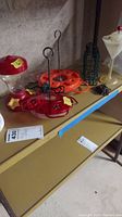 Photo showing various bird feeders on a shelf against a concrete wall, including red feeders, an orange feeder, a metal suet cage, and a white funnel feeder.