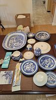 Full set of blue and white Delft china and serving pieces displayed on table plus boxed cheese slicer and decorative tile and shoe.