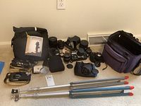 Overview of two tripods, camera bodies, lenses, bags on floor