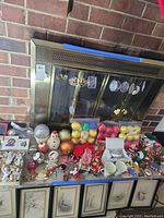 Overview of Christmas decorations displayed on and in front of fireplace, includes ceramic angels, boxes of ornaments, assorted balls, mugs