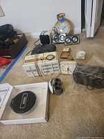 Photo of various clocks, radios, and thermometers arranged on floor, including vintage travel alarm clocks and General Electric radios.