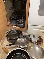 Photo of cookware inside cabinet showing pots and pans, some with glass lids, arranged.