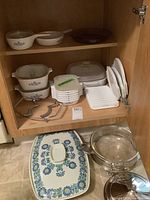 Shelf with white Corning casserole dishes with blue floral pattern, glass covered and uncovered dishes, small glass Corning dishes, and metal serving stand with glass insert