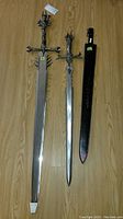 Both decorative swords laid out on a wooden floor. The larger sword has a black sheath sitting next to it.