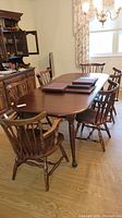 Photo of cherry wood dining table surrounded by six chairs showing overall set and condition.