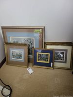 Seven framed Parisian artworks arranged on the floor showing varying frame styles and matting colors, mostly gold frames.