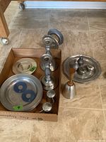 Wide view of most items in the lot including candlestick holders, metal plates, bell, and napkin holder.