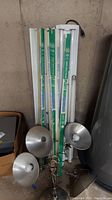 Photo showing 4 aquarium plant grow fluorescent bulbs and 2 shop light fixtures stored vertically against wall with 5 clamp-on lights placed nearby.