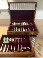 Open wooden chest showing top rack with silver-plated spoons and forks