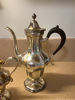 Full view of coffee pot showing lobed body, gooseneck spout, hinged lid with flame finial, and wood handle