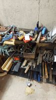 Wide photo showing various hand tools arranged on shelves including saws, clamps, wrenches, hammers, chisels.
