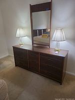 Front angle of nine drawer dresser with mirror and table lamps on top.