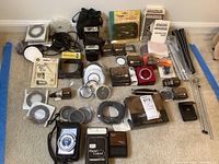 All camera accessories spread on floor showing overall lot contents including flashes, filters, cords, and tripod