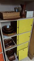 Wood bowls and serving dishes on shelves with yellow cabinet doors and a decorative wood pineapple piece