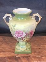 Front view of vase showing floral decoration, two handles, square base, and glazed finish.