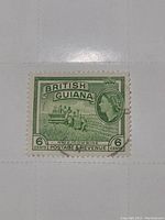 Photo of a British Guiana vintage postage stamp in green color, showing a 6 cent denomination with Queen Elizabeth II portrait and rice combine illustration.