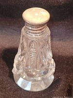 Front angle view of antique crystal salt shaker with detailed cut patterns and silver top showing holes for dispensing.