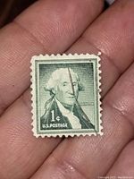 Close-up image of front side of 1 cent George Washington U.S. postage stamp held in hand showing details of printing and wear.