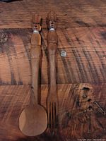 Pair of hand carved wooden salad tongs on a wooden surface with a coin for scale, spoon and fork ends visible along with carved handles.