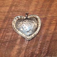 Front side of vintage heart-shaped metal pendant showing embossed floral and sunburst pattern.