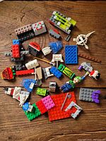 Photo showing a variety of Lego bricks, plates, minifigures, and accessory pieces spread on a wooden surface.