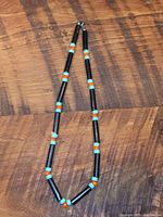 Full view of vintage tribal costume necklace showing alternating black cylindrical beads with round turquoise and red beads on wooden surface.