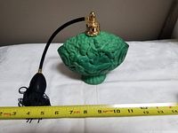Front view of green jade malachite glass perfume bottle with gold-tone atomizer and black tassel, showing floral detailed relief and measuring tape for scale.