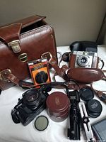 Full lot view showing Minolta X-700, Dacora camera, carrying case, lenses, and accessories spread on surface.