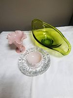 Three glass items shown: pink ruffled pedestal vase, green asymmetrical bowl, and clear round ashtray.