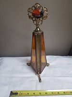 Front view of the vintage amber glass and ornate metal perfume bottle with faux gem stopper, showing size with measuring tape at base.