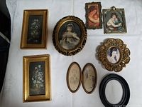 Nine miniature portrait pieces arranged on white fabric, showing variety of frames and subjects including paintings and photographs.