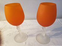 Photo of two vintage Murano mid century hand blown wine glasses with frosted twisted stems and vibrant frosted orange bowls on a white tablecloth.