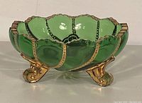 Side view showing the scalloped emerald green glass with gilded edging and three decorative gold-colored feet.