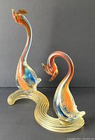 Photo of two Murano glass swans figurines with clear textured base, showing orange and blue accents within the glass.