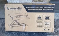 Box showing PrimeCables Sit To Stand Vertical Height Adjustable Desk Riser and product image with color Black.