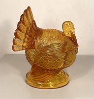Front left side view of the golden amber glass turkey candy dish showing detailed feather patterns and textured body.