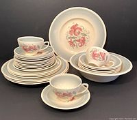Full view of all dinnerware pieces stacked and arranged including plates, bowls and tea cups, showcasing the pink tiger lily design on cream-colored china with light blue border.