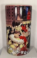 Front view of the cylindrical vintage umbrella stand showing Moulin Rouge design with crowd of elegantly dressed people and a red windmill.