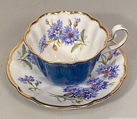 Teacup placed on saucer showing detailed floral design inside and on saucer, gold trim visible.