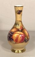 Front view of the porcelain bud vase showing detailed hand-painted peaches, blackberries, and grapes with gold accents at the rim and base.