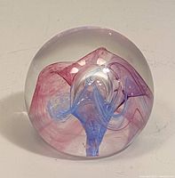 Paperweight showing swirl of pink and blue ribbons inside clear glass sphere, glossy finish, 2 inches high.