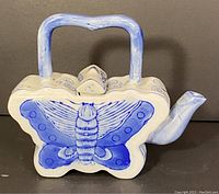 Front view of vintage butterfly-shaped blue and white ceramic teapot showing butterfly wing details and rectangular handle.