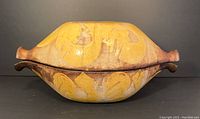 Side view of oval yellow glazed ceramic clay baker with lid showing decorative patterns and minor wear