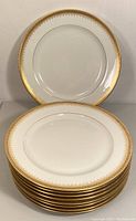 Stack of 8 white porcelain salad plates with gold ornate borders.