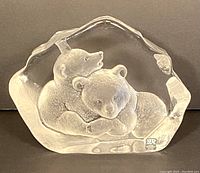 Front view of the clear glass sculpture depicting two frosted bears resting together, showing the signature sticker on the bottom right corner.