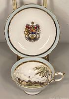 Close-up of saucer showing Canadian coat of arms emblem and tea cup showing outdoor theatre scene with trees and clouds