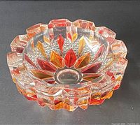 Side angled view showing the triangular red and orange glass accents within the clear cut glass ashtray and scalloped rim design.