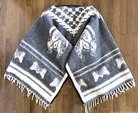Full view of the folded poncho showing the horse design and checked pattern in grey and white wool fabric.